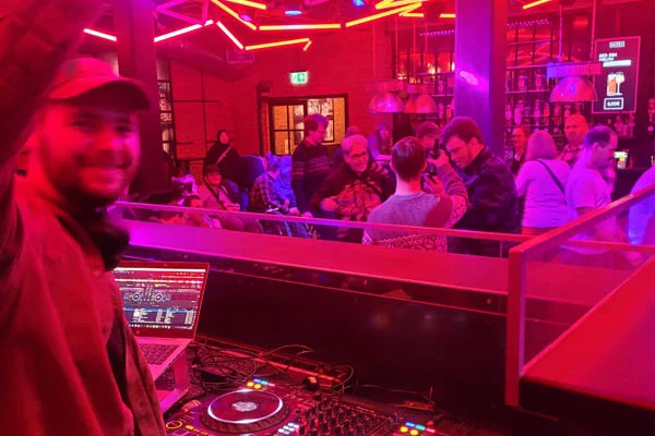 Wahlveranstaltung Ein DJ steht am DJ-Pult und Personen im Hintergrund feiern.