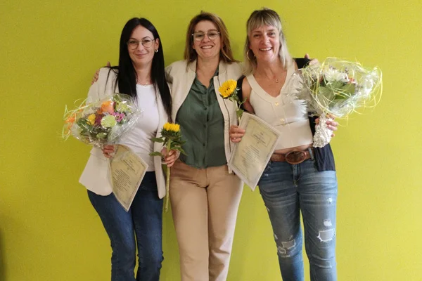 das foto zeigt drei junge frauen, zwei haben blumensträuße in der hand