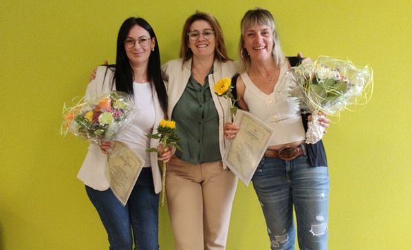 das foto zeigt drei junge frauen, zwei haben blumensträuße in der hand