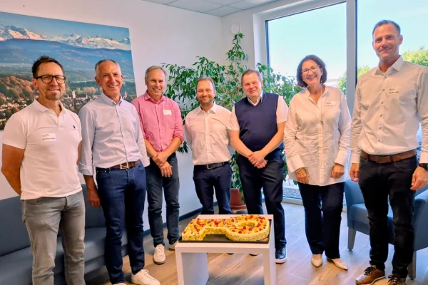 Mehrere Personen stehen um einen Kuchen in Schlüssel-Form und schauen in die Kamera.