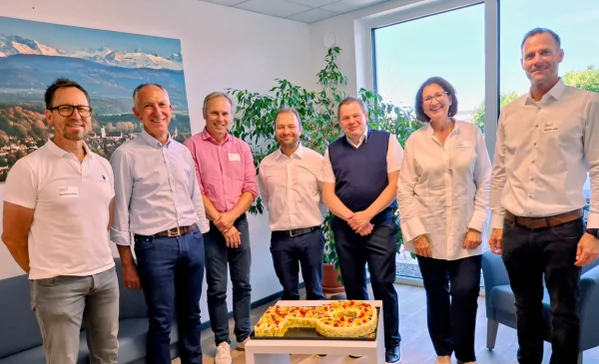 Mehrere Personen stehen um einen Kuchen in Schlüssel-Form und schauen in die Kamera.