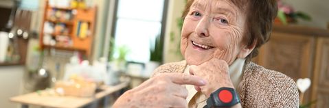 Das Bild zeigt eine Frau in ihrem Wohnzimmer mit einem Notrufarmband