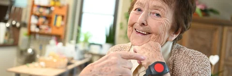Das Bild zeigt eine Frau in ihrem Wohnzimmer mit einem Notrufarmband