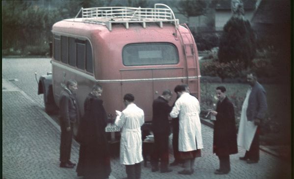 Ein altes Foto mit einem roten Bus und Personen davor.