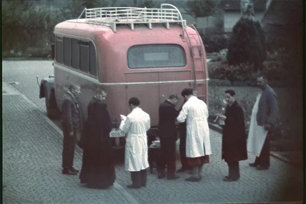 Ein altes Foto mit einem roten Bus und Personen davor.