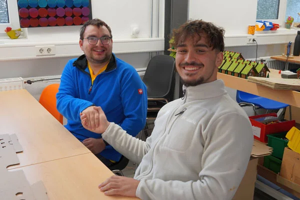 Zwei Personen sitzen an einem Tisch und schütteln sich die Hand.