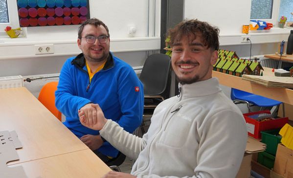 Gemeinsames Arbeiten Zwei Personen sitzen an einem Tisch und schütteln sich die Hand.