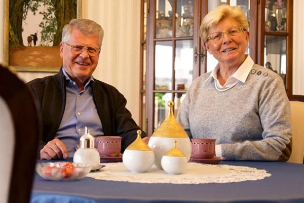 Ursula und Karl Volk in ihrem Zuhause Das Bild zeigt ein älteres Ehepaar, das gemeinsam am Kaffeetisch sitzt und sich unterhält.