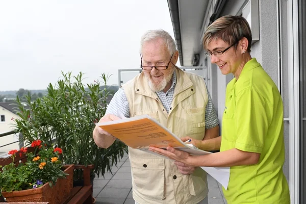 Das Bild zeigt einen Mann und eine Frau auf einem Balkon, ein Dokument lesend