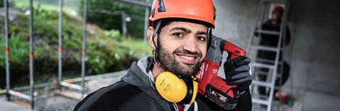 Das Bild zeigt im Vordergrund einen Mann mit orangenem Helm der vor einer Leiter steht und außerdem verlinkt das Bild zum Arbeitgebervideo der Technik