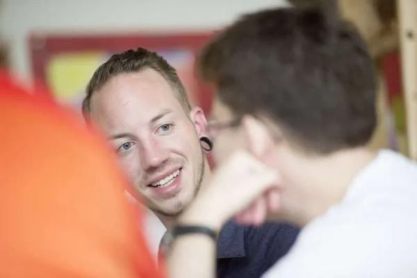 Das Bild zeigt zwei Männer die sich unterhalten und einer von ihnen schau in die Kamera.