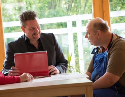 Das Bild zeigt zwei Personen an einem Schreibtisch mit Unterlagen
