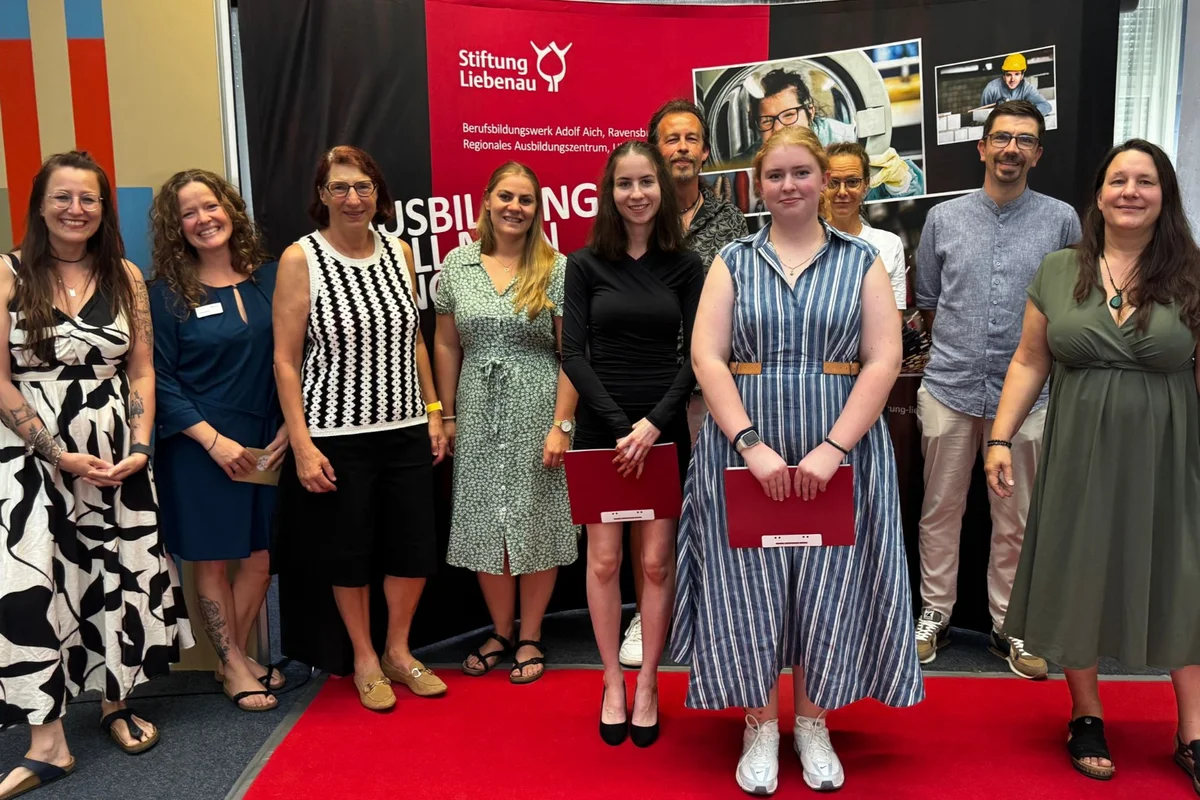 Absolventenfeier Gruppenbild einiger Absolventen vor einem Stiftung Liebenau Aufsteller.