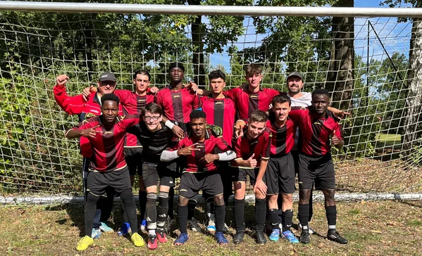 BBW Ravensburg Vizemeister Zwölfköpfiges Fußballteam in roten und schwarzen Trikots posiert lächelnd und jubelnd vor einem Tornetz im Freien, Bäume im Hintergrund.