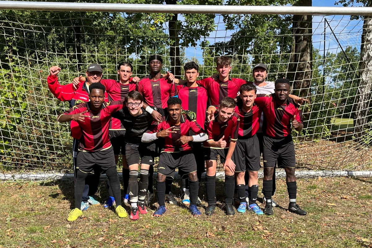 BBW Ravensburg Vizemeister Zwölfköpfiges Fußballteam in roten und schwarzen Trikots posiert lächelnd und jubelnd vor einem Tornetz im Freien, Bäume im Hintergrund.