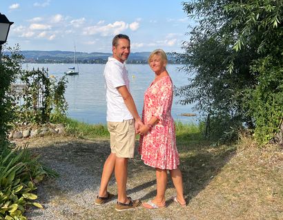 das bild zeigt ein etwas älteres paar, das händchen haltend vor dem bodensee steht.