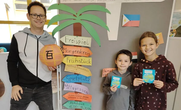 Ein Erwachsener und zwei Kinder schauen in die Kamera und zeigen, was sie gebastelt haben.