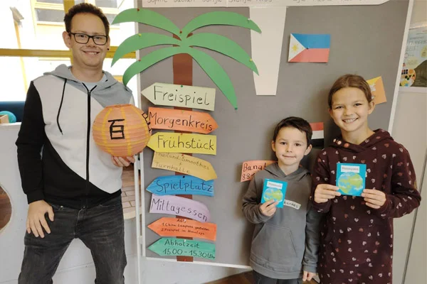 Ein Erwachsener und zwei Kinder schauen in die Kamera und zeigen, was sie gebastelt haben.