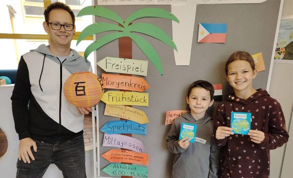 Ein Erwachsener und zwei Kinder schauen in die Kamera und zeigen, was sie gebastelt haben.