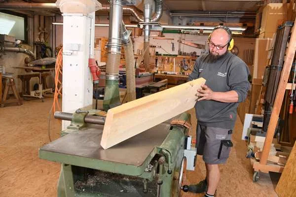 Das Bild zeigt einen bärtigen Mann de gerade ein Holzbrett bearbeitet
