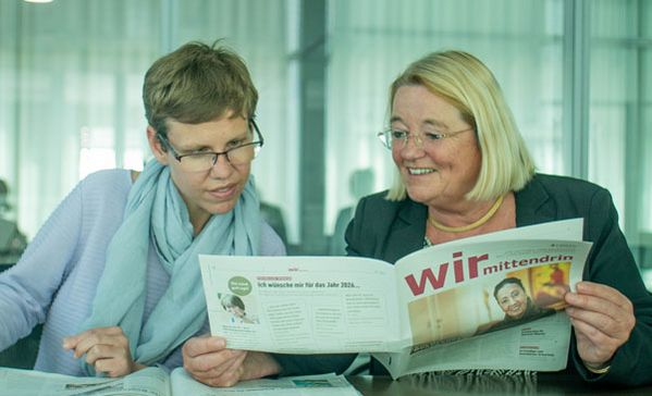 Zwei Frauen sitzen an einem Tisch und schauen in eine Zeitung.