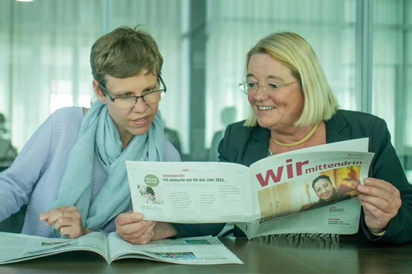 Zwei Frauen sitzen an einem Tisch und schauen in eine Zeitung.