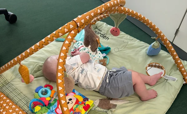 Das Baby Linus liegt auf einer Decke und spielt mit seinen Kuscheltieren.