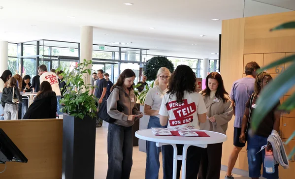 Mehrere Personen stehen in Gruppen um Stehtische und reden miteinander.