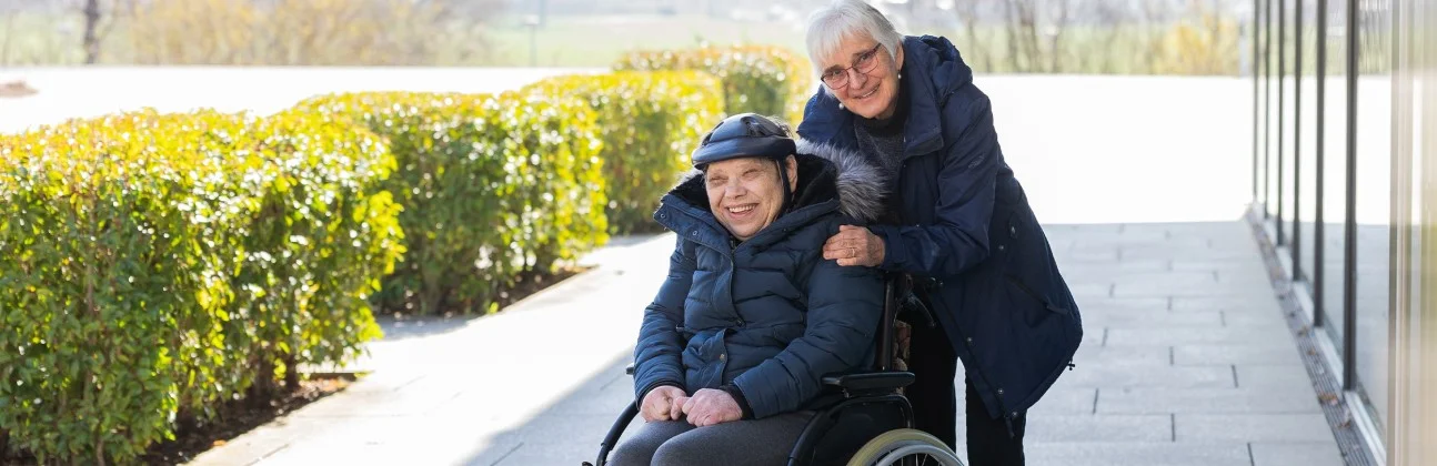 Ehrenamt bei der Stiftung Liebenau Das Bild zeigt zwei Personen. eine von ihnen sitzt im Rollstuhl und gemeinsam schauen sie in die Kamera