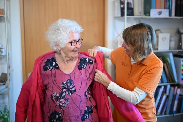Das Bild zeigt eine Frau, die einer anderen Frau in den Mantel hilft