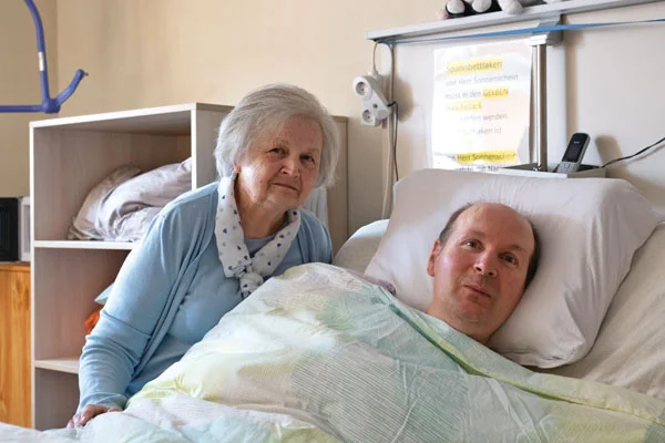 Suizidversuch Ein Mann liegt in einem Bett und eine Frau sitzt daneben.