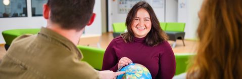 Das Bild zeigt eine junge Frau mit einer Weltkugel in der Handmit zwei weiteren Personen