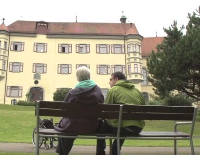 Das Bild zeigt zwei Personen auf einer Bank mit Blick auf das Schloss Liebenau