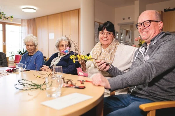 Die bedeutende Kraft des Ehrenamtes Das Bild zeigt mehrere Personen die gemeinsam an einem tisch sitzen und mit Zweigen etwas basteln