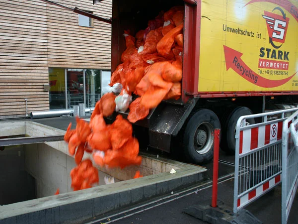 2,1 Millionen Windeln werden jährlich entsorgt Bild eines Müllwagens, der orangene Windeln in einen Container schüttet.