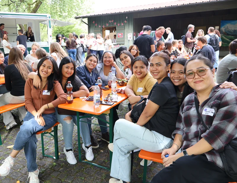 Einführungstag 2026 Viele Personen sitzen im Freien an Biertischen und unterhalten sich. Der vordere Tisch mit vielen Frauen lächelt in die Kamera.