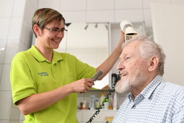Das Bild zeigt eine Frau, die einem Mann die Haare fönt
