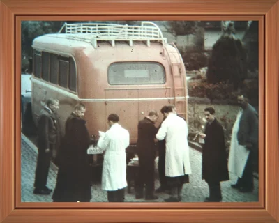 1939, Ermordung von Menschen mit Behinderungen. Entgegen christlichen Überzeugungen werden Menschen mit Behinderungen und psychischen Erkrankungen in der NS-Zeit diskriminiert und verfolgt. Ab 1934 müssen Bewohnerinnen und Bewohner aus Liebenau in umliegenden Krankenhäusern zwangssterilisiert werden. 1939 erreicht die Anstalt ein Fragebogen eines Wissenschaftlers, in welchem nach der Haltung zur sogenannten „schmerzlosen Vernichtung von Geistestoten“ gefragt wird. Direktor Wilhelm äußert in seiner Antwort deutlich die prinzipielle Ablehnung solcher Maßnahmen und bezeichnet sie als „wilde Barbarei“ und „bestialisch“. Die Frage, ob es in seiner Heil- und Pflegeanstalt „Geistestote“ gäbe, beantwortet er schlicht mit „nein!“.  Ab Anfang 1940 werden in der „Aktion T 4“ zehntausende Menschen mit Behinderungen gezielt ermordet. Am 1. Juli 1940 beginnen massenhafte Deportationen aus Liebenau. Bis Mitte März 1941 wird ein großer Teil der Bewohnerinnen und Bewohner aus den Liebenauer Einrichtungen mit Bussen abgeholt und in die Tötungsanstalten Grafeneck und Hadamar gebracht. Insgesamt finden mehr als 500 Menschen aus Liebenau den Tod. Zu den „Euthanasie“-Opfern der Liebenauer Einrichtungen gehören auch die Bewohnerinnen und Bewohner jüdischer Herkunft.  Unter dem Vorwand, dass die Pfleglinge unentbehrlich für die Arbeit in der Liebenauer Landwirtschaft seien, versucht Direktor Wilhelm die Transporte zu verhindern – vergebens. Rettungsversuche gelingen jedoch im kleinen Rahmen: Einige Menschen mit Behinderungen werden als Hilfskräfte angestellt oder als Pensionäre eingestuft. Manche werden offiziell entlassen, verbleiben jedoch in Liebenau, andere werden gar nicht erst im Aufnahmebuch vermerkt.. Das Bild zeigt Menschen aus Liebenau bei der Abholung durch den roten Bus.