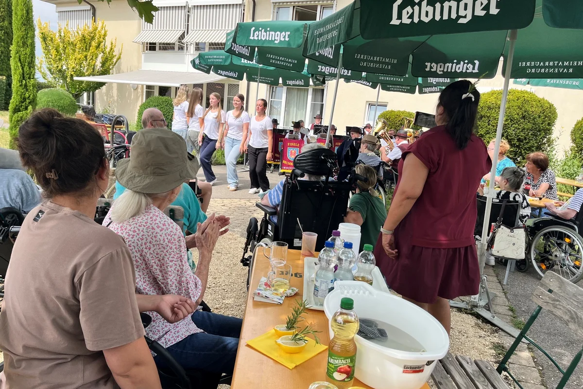 Sommerfest Im Hintergrund ist eine Tanzgruppe und im Vordergrund Zuschauerinnen und Zuschauer zu sehen.