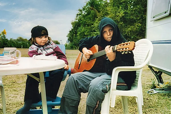 das bild zeigt zwei kinder an einem tisch, ein kind spielt gitarre