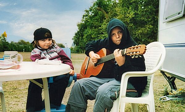 das bild zeigt zwei kinder an einem tisch, ein kind spielt gitarre