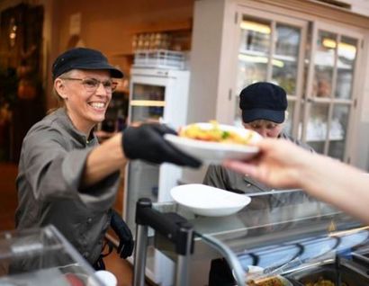 Das Bild zeigt eine Frau an einer Essensausgabe