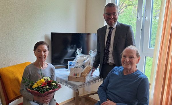 Eiserne Hochzeit Ein Ehepaar mit einem Blumenstrauß und ein Mann lächeln in die Kamera.