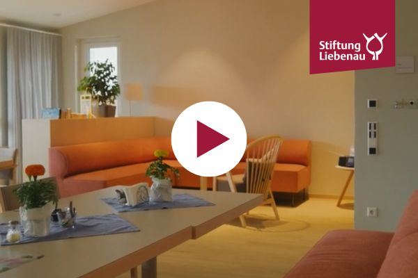 Video vom Hospiz Ein Foto vom Wohnzimmer und ein Playbutton in der Mitte des Bilds.