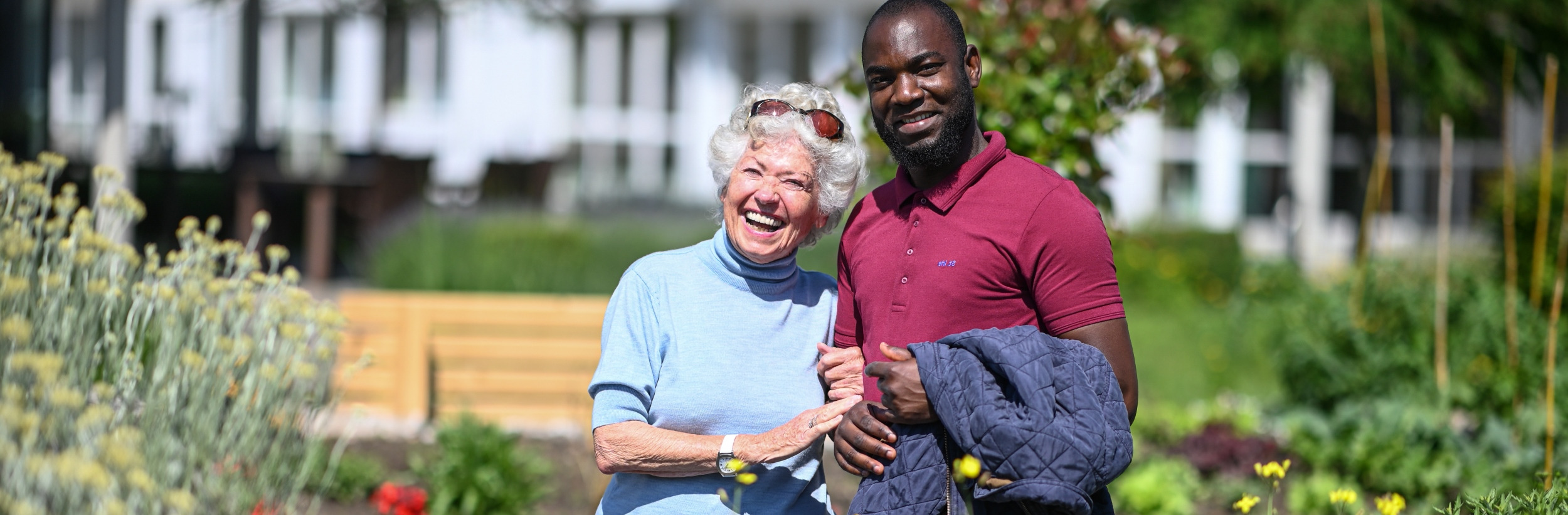 Das Bild zeigt eine ältere Dame und einen Pfleger in einem Garten