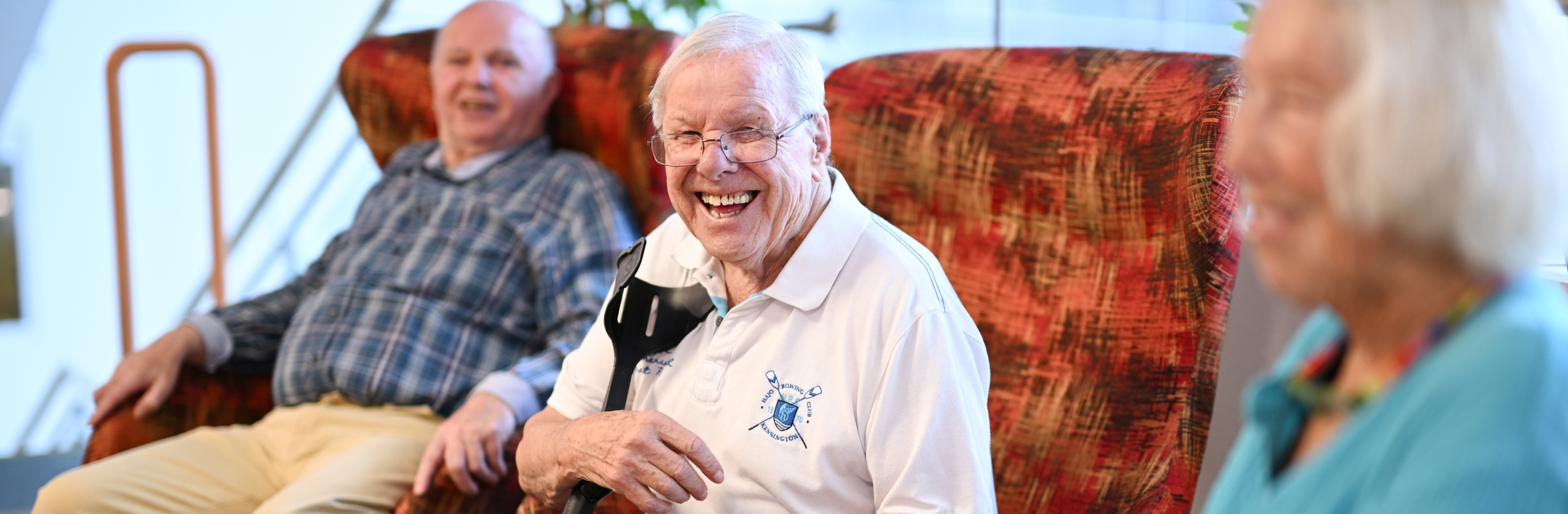 Das Bild zeigt zwei ältere Männer und eine ältere Frau auf einer Couch