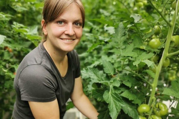 Das Bild zeigt eine junge Frau neben einer Tomatenstaude
