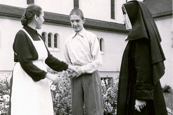 Das Bild zeigt ein Ordensschwester, eine Krankenschwester und einen Bewohner im Garten