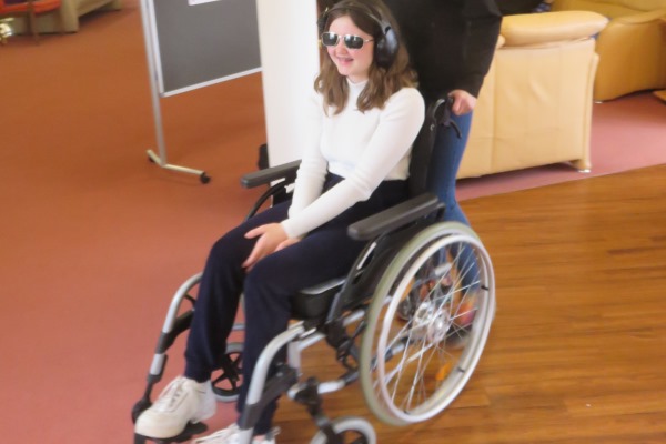 Das Bild zeigt eine Schülerin im Rollstuhl mit Kopfhörern