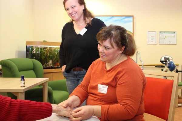 Mit sanften Bewegungen massiert die Pflegefachkraft Heike Kreidel (vorne) die Hand einer Heimbewohnerin, während sich Einrichtungsleiterin Yvonne Denzel (stehend) mit ihr unterhält. 